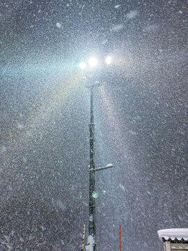 VERTICAL: A street lamp shines brightly amidst a heavy snowfall, providing a beacon of light on a stormy winter night. A flurry of snowflakes engulfs the mountains of Hokkaido on a cold winter night.