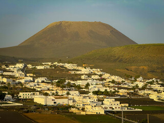 Traditional whitewashed village lies at the base of a volcanic mountain on Lanzarote. Stunning contrast between white buildings and dark, rugged volcanic landscape typical of the Canary Islands. © helivideo