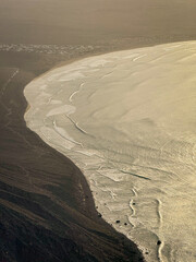 Volcanic island coastline where dark, rugged land meets Atlantic Ocean. Waves rolling along Famara beach create mesmerizing patterns on the sea surface. Stunning view of famous surf spot at Lanzarote.