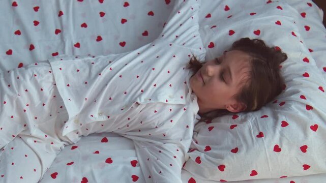 An 11 year old girl wakes up in the morning in her bed wearing heart-shaped pajamas and stretches.