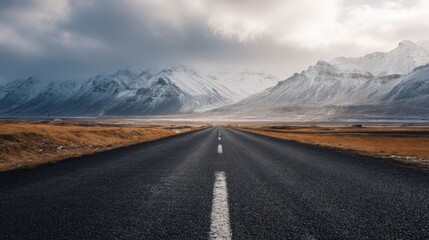 Straight road in Iceland leading toward snow-capped mountains under cloudy sky, winter landscape of nature and adventure, travel and exploration across vast open scenery toward an unknown horizon.
