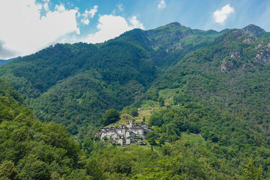 Charming, traditional village with granite buildings and a church steeple is nestled amidst a green mountain valley where lush forests cover the slopes. Picturesque alpine landscape in Swiss Alps.
