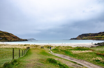 Coastal path to a sandy beach on the Isle of Mull, Scotland, with dunes and fence posts under overcast skies. Minimal seascape with leading lines and copy space.
