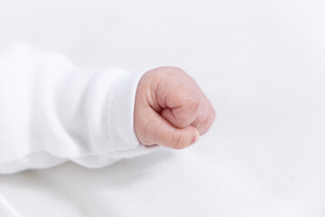 Close up of a newborn baby hand clenched into a fist with white sleeve on white background symbolizing new life
