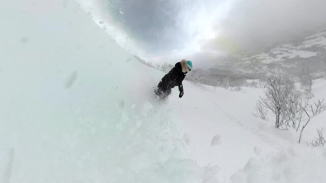 SELFIE: Snowboarder descends a pristine alpine slope, carving smoothly through deep powder snow. Snowy trees and winter landscape highlight the thrill and freedom of snowboarding in untouched terrain.