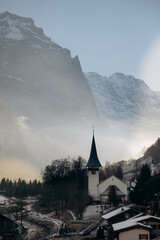 Lauterbrunnen village in winter: a dark and atmospheric mountain scenery. Moody winter landscape of Lauterbrunnen valley with sun rays through the mist.