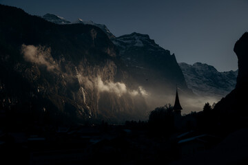 Lauterbrunnen village in winter: a dark and atmospheric mountain scenery. Moody winter landscape of Lauterbrunnen valley with sun rays through the mist.