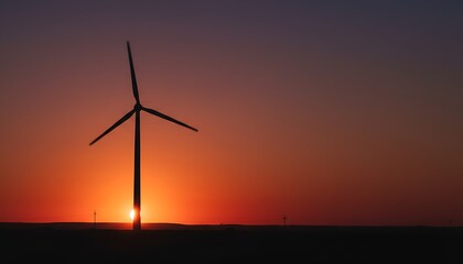 Obraz premium A wind turbine stands silhouetted against a vibrant sunset in a vast landscape.