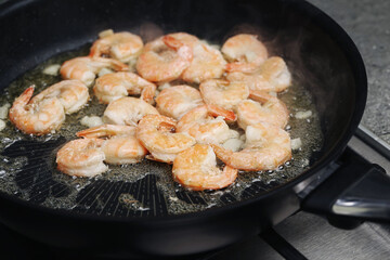 Garlic butter shrimp frying in pan. Prawns cooking in hot skillet. Seafood meal preparation closeup. Fresh shrimp with garlic and butter. Homemade dinner cooking background.
