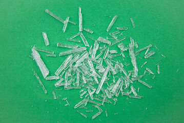 Menthol crystals are a purified, solid form of menthol, white crystalline shards scattered on green background.