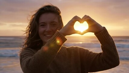 Cinematic 4K Slow Motion of a Happy Young  croWoman Making a Heart Shape with Hands Framing the Setting Sun on a Beach - Powered by Adobe