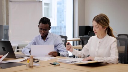 Diverse business people managing workflow by checking records, processing materials, and stamping forms at an office table - Powered by Adobe