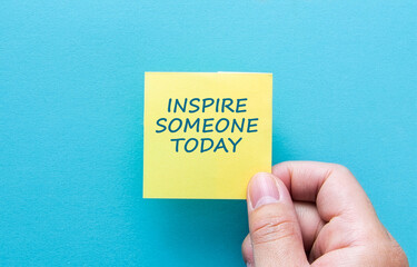 Hand holding sticky note with inspire someone today message