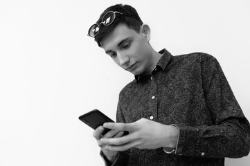Young man engaged with smartphone while wearing sunglasses indoors near plain wall