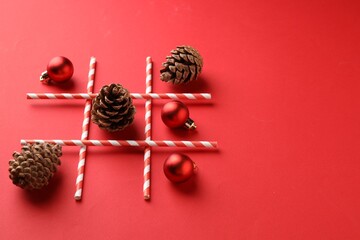 Tic tac toe game made with Christmas balls and cones on red background. Space for text
