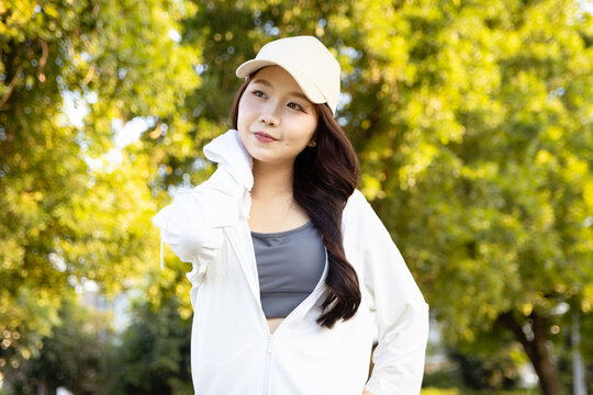 Happy beautiful woman wipes sweat with towel while take a break after jogging exercise in park. Asian girl relaxing amidst green nature after running work out outside Fitness female runner outdoor