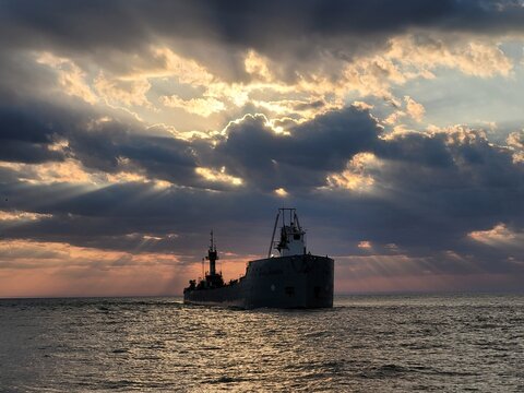 Cargo vessel silhouette on water at dramatic sunset