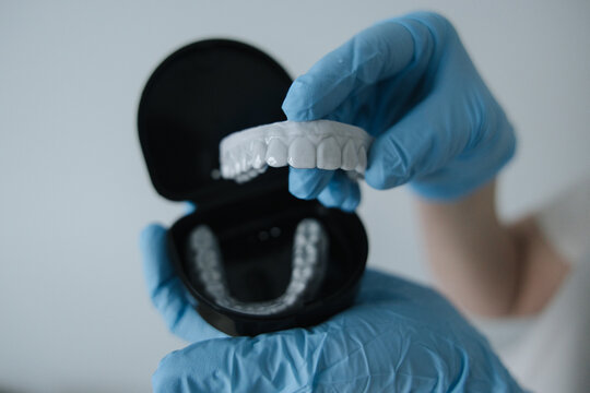 Dental aligner held in blue medical gloves above an open case. Concept of modern dentistry, orthodontic care and oral hygiene.