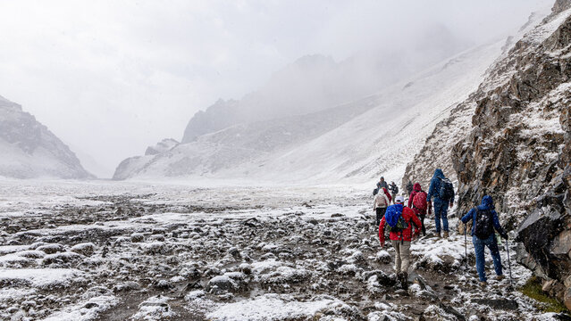 A group of tourists with backpacks are marching along a snowy mountain trail. The view from the back.