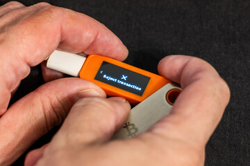 Caucasian hands holding hardware wallet with reject transaction message in dark indoor setting with artificial light.