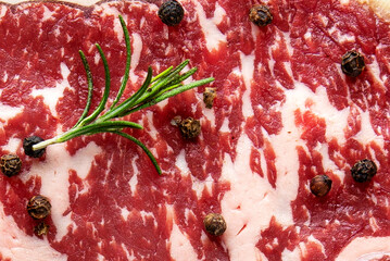 Raw Marbled Beef Steak Background with Fresh Rosemary and Black Peppercorns