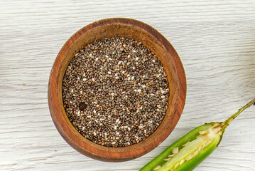 Organic Raw Chia Seeds in Wooden Bowl with Green Chili Pepper on White Table