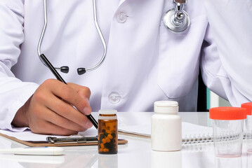 Male Doctor in White Coat Writing Medical Prescription with Stethoscope and Pill Bottles on Desk