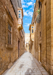 Charming narrow street in Mdina, Malta, lined with historic limestone buildings and traditional balconies.