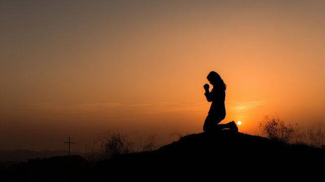 Silhouette of a Woman Praying at Sunset with a Christian Cross on a Hilltop.