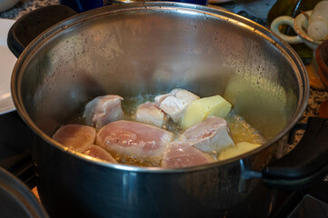 Raw chicken and potatoes cooking in pot
