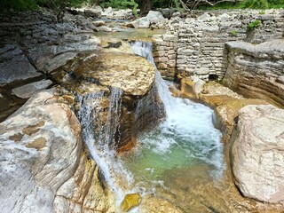 nature made bath, a gentle waterfall cascades over textured rocks into a clear pool surrounded by...