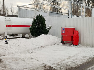 A gas tank at a gas station in winter and a fire safety stand, snow, bad weather, fuel prices