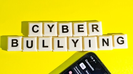 “CYBER BULLYING” spelled out on yellow background with smartphone showing comment section—symbolizing digital abuse and social media toxicity.