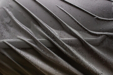 Detail of a dark waterproof fabric surface with raindrops and fabric folds forming sharp diagonal lines.