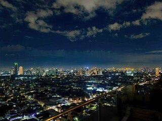 Fototapeta premium Panoramic Night View of a Metropolis Skyline with Glowing City Lights Under Cloudy Sky