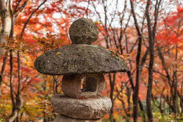 An ancient stone lantern stands amidst a vibrant tapestry of crimson and golden autumn leaves in a tranquil Japanese garden. This serene scene captures the peaceful essence of fall, embodying timeless