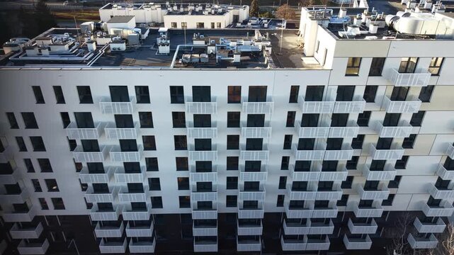 Left-to-right drone flyby of modern apartment building with stacked balconies and flat-roof HVAC systems at golden hour &mdash; residential architecture, urban housing estate, Poland