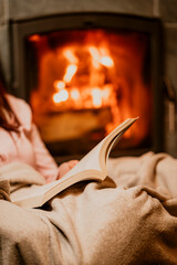 open book with fire,Person reading a book by the fireplace, wrapped in a warm blanket. Cozy home atmosphere with glowing fire, perfect for winter evenings, relaxation, and peaceful comfort.