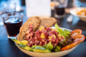 Close-up of a fresh salad bowl with diced ingredients, vegetables, bread slices, and a drink in the background. Colorful, healthy meal served in a cozy dining setting