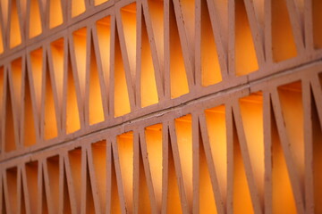 Abstract geometric lattice wall with repeating triangular openings, illuminated by warm orange light, creating depth, rhythm, and a modern architectural pattern background.