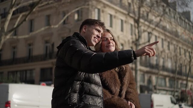 A young couple in Paris France is seen pointing and smiling on a city street The panning shot captures the happy couple enjoying their vacation and sightseeing in European.