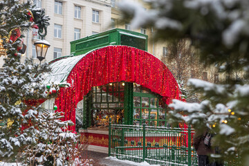 Moscow, Russia - 30 December 2025: Christmas market pavilion with red curtains, fairy lights and snow covered trees in winter city, Moscow, Russia.