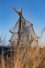 Traditionelle Reusen- bzw. Fischernetze an Holzpf&auml;hlen in den D&uuml;nen am Timmendorfer Strand an der Ostsee. Die leeren Netze h&auml;ngen ruhig im Wind vor blauem Himmel und vermitteln maritimes Handwerk