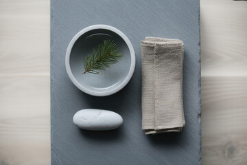 Round gray bowl with green pine sprig, white stone, and beige cloth on slate surface