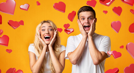 Young couple opens their mouths in amazement and touches their cheeks. They stand in a yellow...