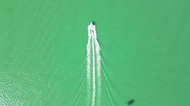 Top down parasailing boat wake on emerald sea. 4K horizontal drone footage shows a speedboat cutting vivid green water near Batumi, Georgia, with white foam trails and visible parachute shadow.