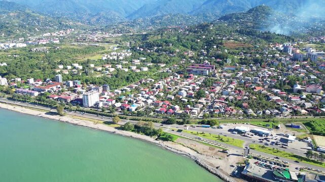 Aerial suburb view near Batumi from sea. 4K horizontal drone footage in clear weather shows residential districts, private houses and a busy road with cars along the Georgian coastline.
