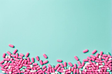 Pink pills scattered on a pastel turquoise background in a minimalist flat lay arrangement.