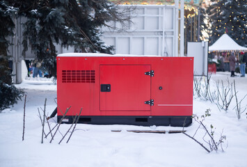 Red industrial backup generator standing in snow outdoors near winter holiday market and carousel.
