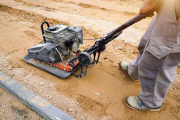 worker rams the ground with a vibrating machine.